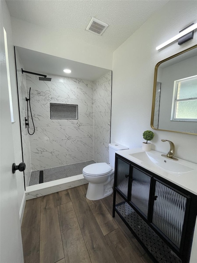 bathroom featuring toilet, wood-type flooring, a textured ceiling, a tile shower, and vanity