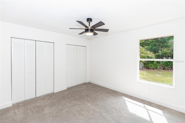 unfurnished bedroom featuring carpet flooring, two closets, and ceiling fan