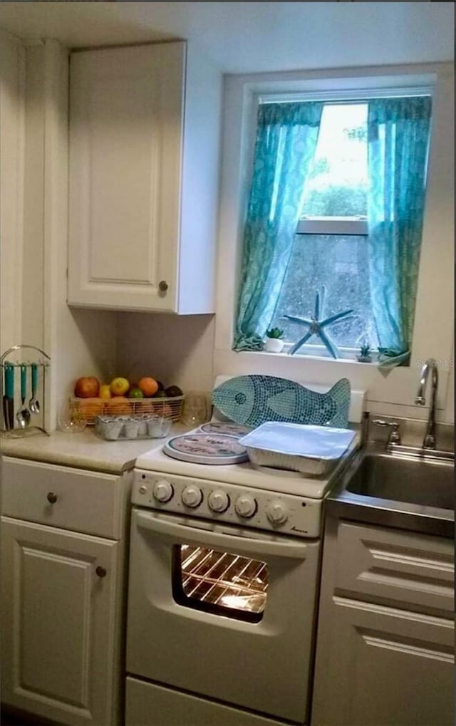 kitchen with sink, electric range, a wealth of natural light, and white cabinets