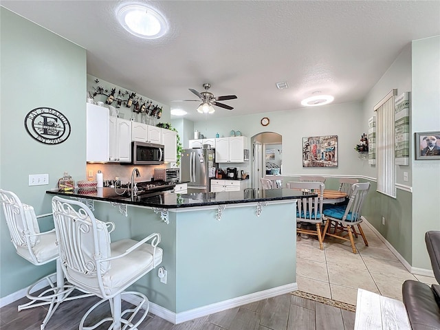kitchen featuring a kitchen bar, stainless steel appliances, a peninsula, white cabinets, and ceiling fan