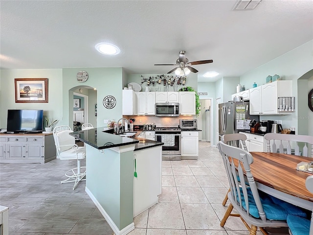kitchen featuring a peninsula, arched walkways, a sink, stainless steel appliances, and dark countertops