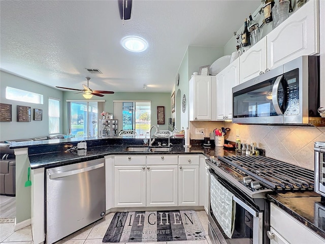 kitchen featuring a sink, open floor plan, white cabinetry, stainless steel appliances, and a peninsula
