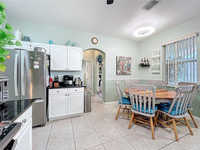kitchen with visible vents, light tile patterned flooring, arched walkways, freestanding refrigerator, and white cabinets