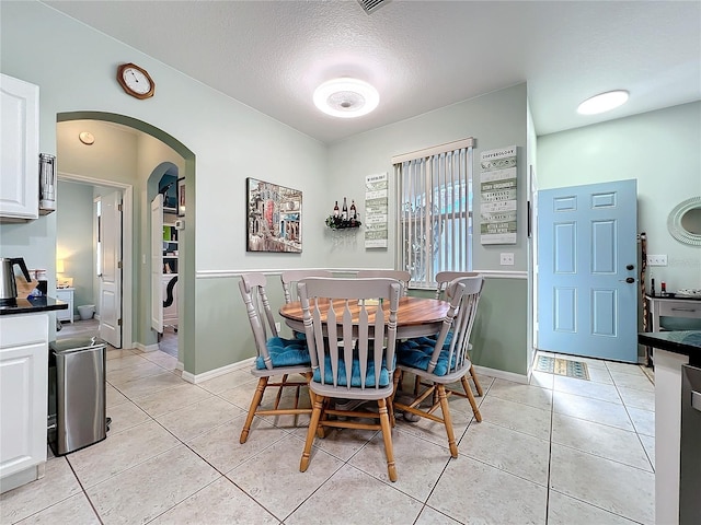 dining area featuring light tile patterned floors, arched walkways, a textured ceiling, and baseboards