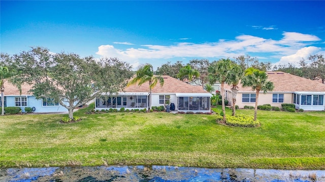 rear view of property featuring a lawn, a water view, a sunroom, and stucco siding