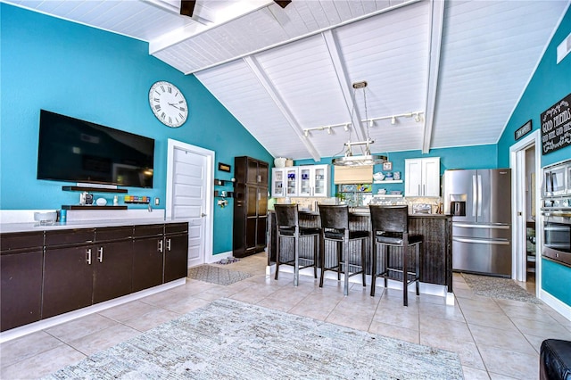 kitchen with appliances with stainless steel finishes, lofted ceiling with beams, dark brown cabinets, and light tile patterned floors