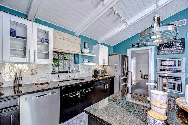 kitchen featuring dark stone counters, lofted ceiling with beams, stainless steel appliances, white cabinetry, and a sink