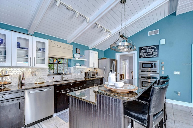 kitchen featuring stainless steel appliances, visible vents, lofted ceiling with beams, a sink, and dark stone countertops