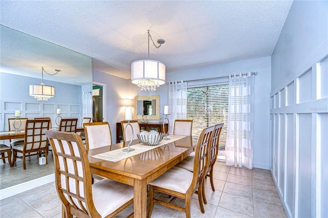 dining area with a chandelier, light tile patterned floors, a textured ceiling, and a decorative wall