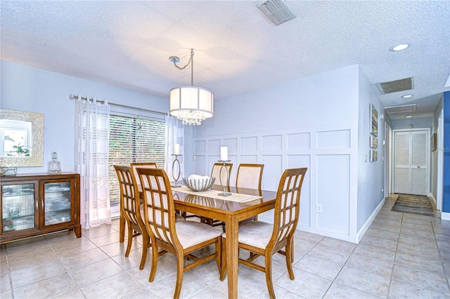 dining room featuring light tile patterned floors, visible vents, a decorative wall, and a textured ceiling