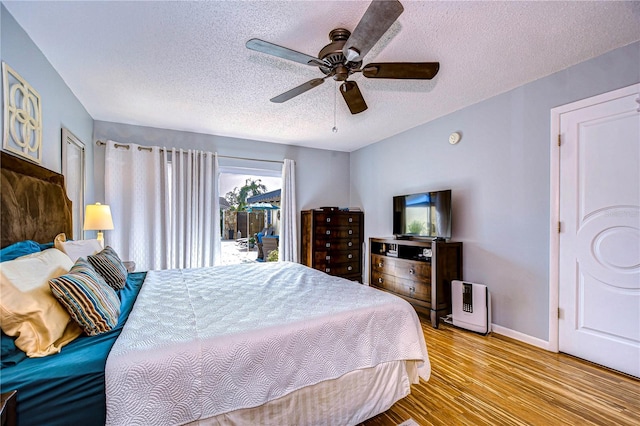 bedroom featuring a textured ceiling, ceiling fan, wood finished floors, access to exterior, and baseboards