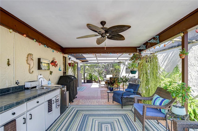 view of patio / terrace with glass enclosure, area for grilling, a sink, a ceiling fan, and exterior kitchen