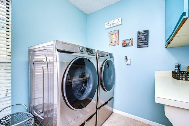 laundry area featuring light tile patterned floors, a textured ceiling, baseboards, washer and dryer, and cabinet space