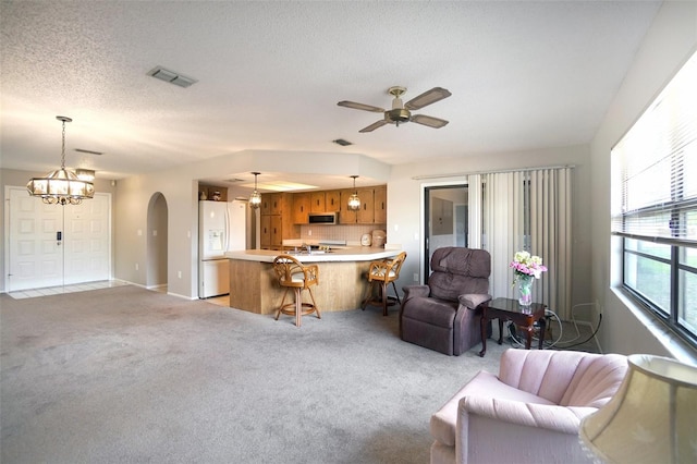 living room featuring a textured ceiling, arched walkways, light carpet, ceiling fan with notable chandelier, and visible vents