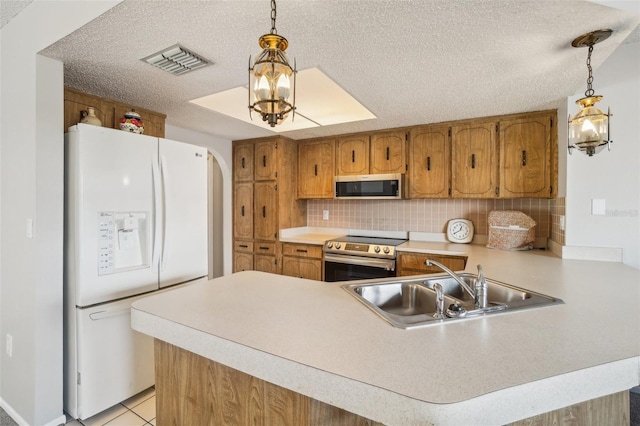 kitchen featuring stainless steel appliances, visible vents, brown cabinetry, a sink, and a peninsula