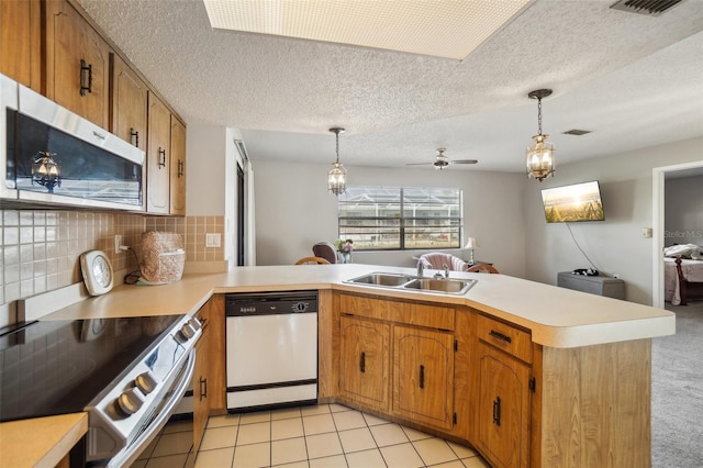 kitchen featuring stainless steel appliances, light countertops, a sink, and a peninsula