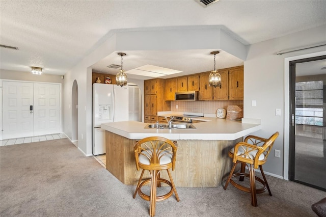 kitchen featuring light colored carpet, light countertops, brown cabinets, white fridge with ice dispenser, and stainless steel microwave