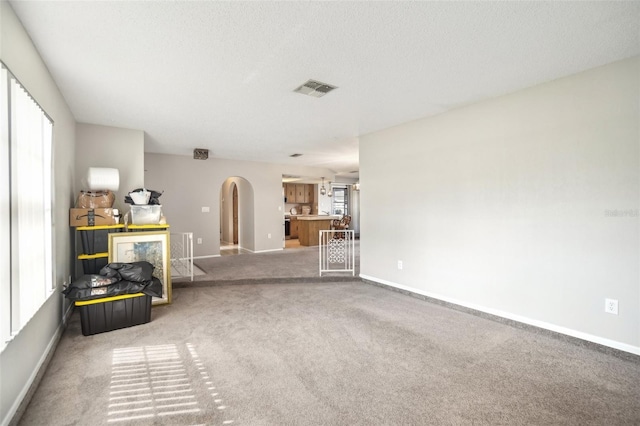 unfurnished living room featuring a wealth of natural light, arched walkways, visible vents, and carpet floors