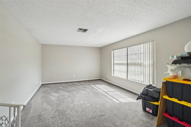 spare room featuring baseboards, a textured ceiling, visible vents, and carpet flooring