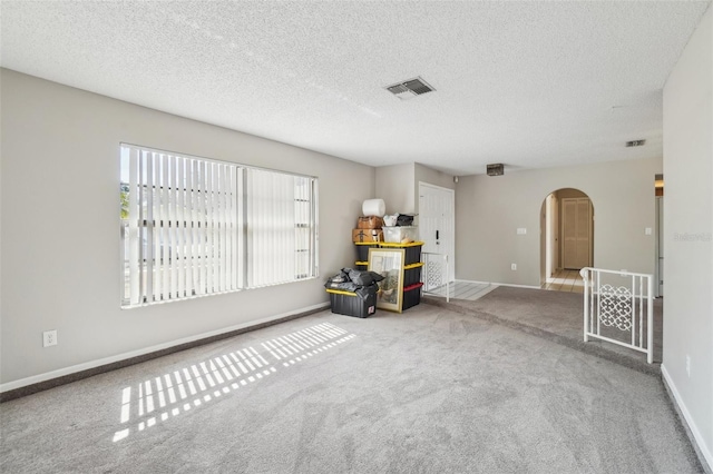 interior space featuring arched walkways, a textured ceiling, carpet floors, visible vents, and baseboards