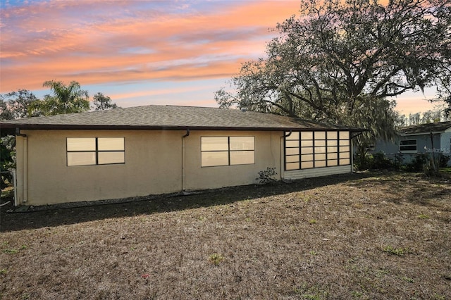 view of property exterior with a shingled roof, a lawn, and stucco siding