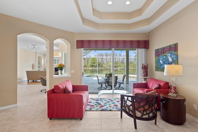 living area featuring arched walkways, a tray ceiling, recessed lighting, light tile patterned flooring, and baseboards