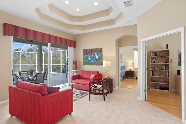 living area featuring baseboards, visible vents, a raised ceiling, arched walkways, and a sunroom