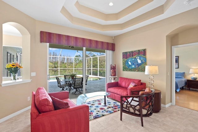 living room featuring a sunroom, baseboards, a tray ceiling, and tile patterned floors