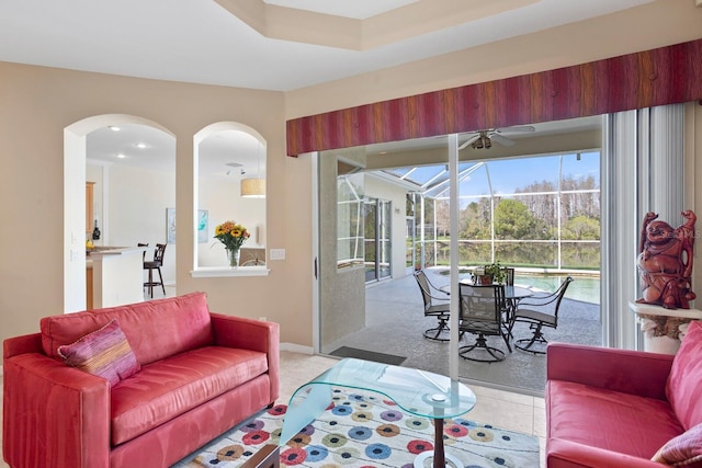 living area featuring arched walkways, a sunroom, light colored carpet, and baseboards