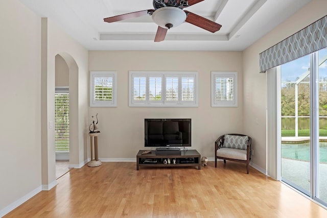 sitting room with arched walkways, baseboards, a raised ceiling, a ceiling fan, and light wood-style flooring