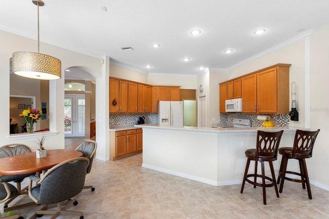 kitchen featuring a peninsula, white appliances, light countertops, and brown cabinetry