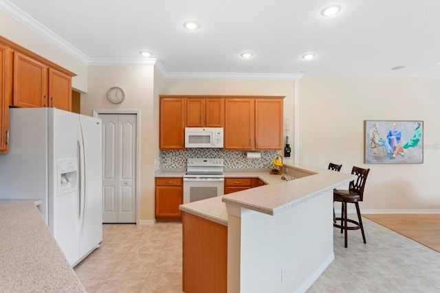 kitchen with a peninsula, white appliances, a breakfast bar, light countertops, and ornamental molding