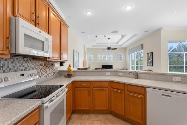 kitchen with a tray ceiling, light countertops, brown cabinetry, a sink, and white appliances