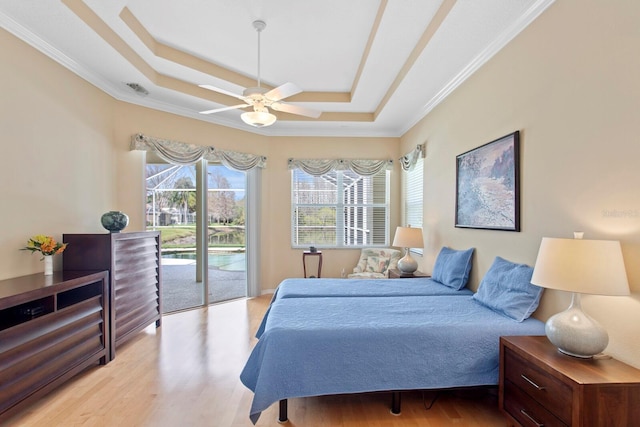 bedroom featuring ornamental molding, access to outside, a tray ceiling, and wood finished floors