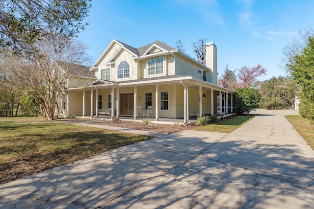 view of front of home with driveway, a chimney, a front lawn, and a porch