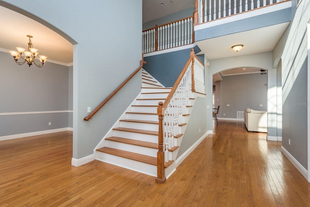 stairs with arched walkways, hardwood / wood-style floors, ornamental molding, and baseboards