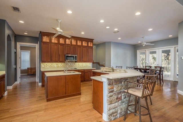 kitchen featuring a sink, visible vents, backsplash, stainless steel microwave, and an island with sink