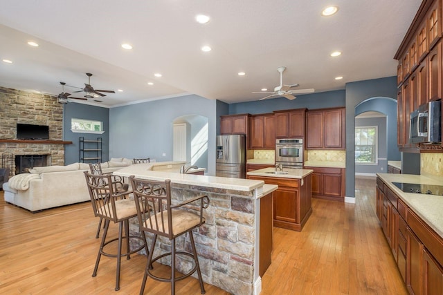 kitchen with arched walkways, decorative backsplash, an island with sink, ceiling fan, and appliances with stainless steel finishes