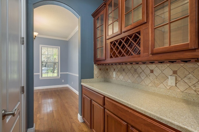 bar featuring arched walkways, light wood-style flooring, baseboards, tasteful backsplash, and crown molding