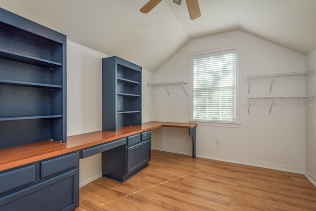 home office featuring light wood finished floors, ceiling fan, vaulted ceiling, and built in desk