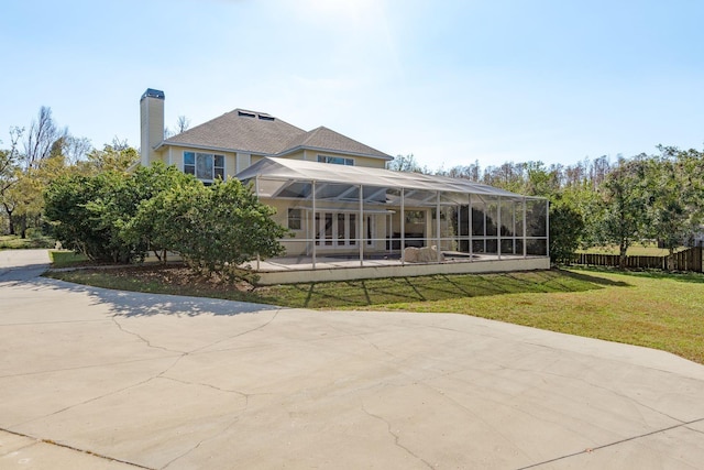 rear view of property featuring a lawn, a patio, a chimney, a lanai, and fence