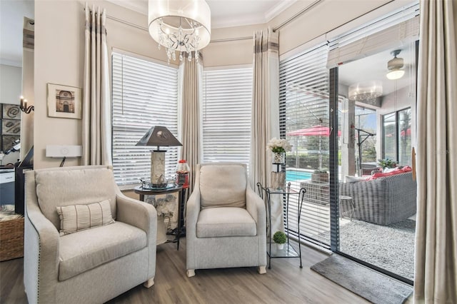 living area with ornamental molding, hardwood / wood-style floors, and an inviting chandelier