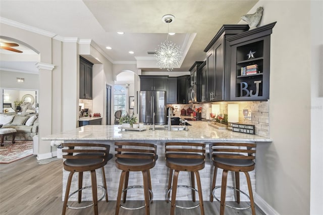 kitchen with appliances with stainless steel finishes, tasteful backsplash, light stone countertops, kitchen peninsula, and light wood-type flooring