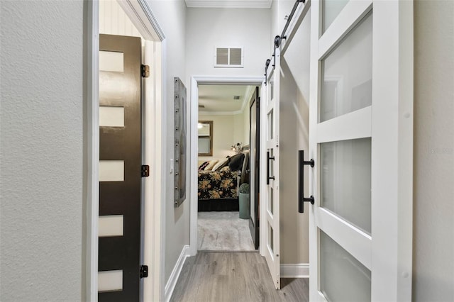 hall featuring wood finished floors, ornamental molding, baseboards, and visible vents