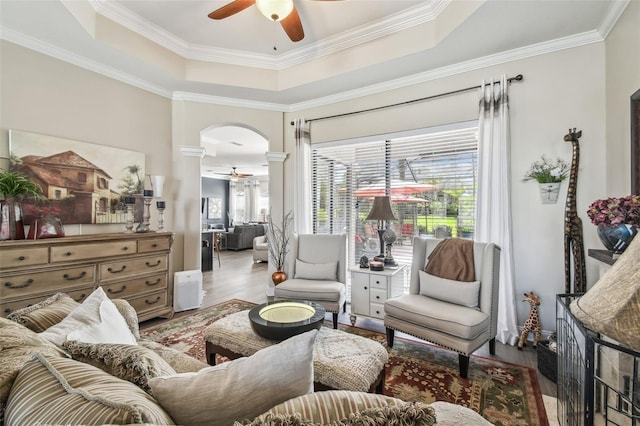 living area with arched walkways, a tray ceiling, wood finished floors, and a ceiling fan