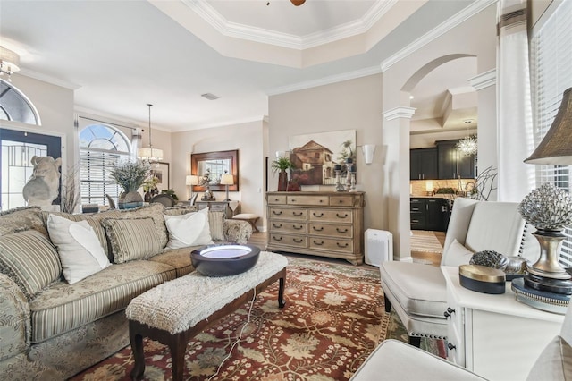 living room featuring decorative columns, arched walkways, ornamental molding, and a chandelier