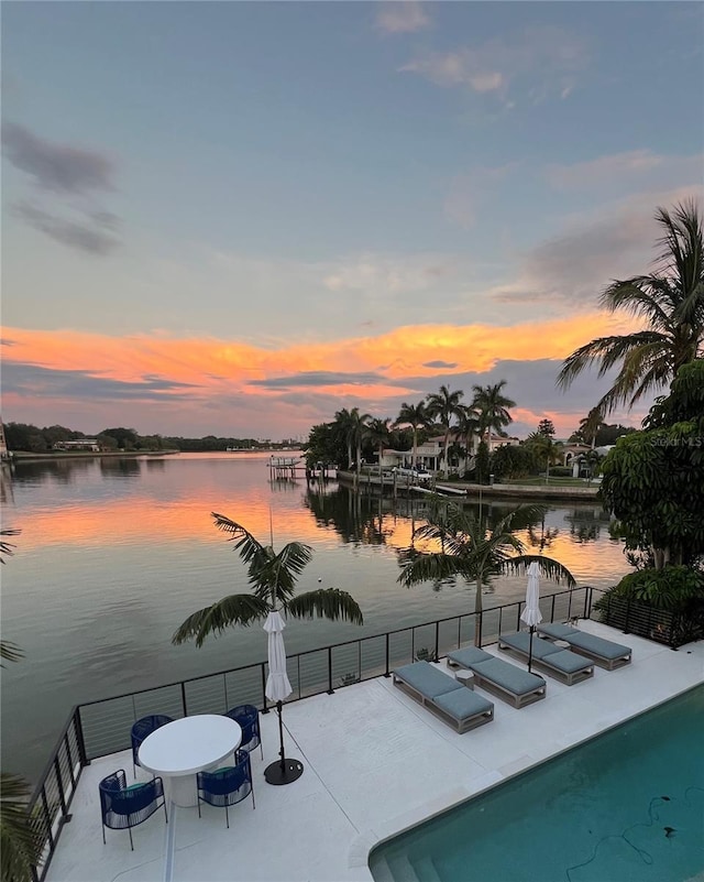 pool at dusk with a patio area and a water view