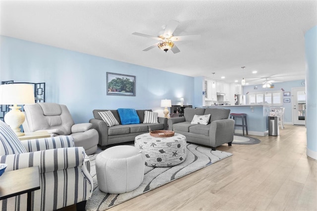 living room with ceiling fan, a textured ceiling, and light wood-type flooring