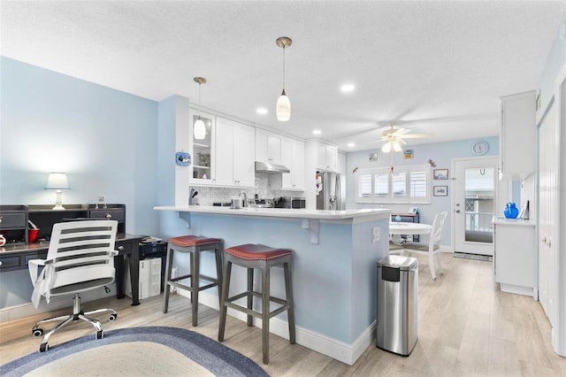 kitchen featuring pendant lighting, stainless steel fridge, a breakfast bar area, white cabinets, and kitchen peninsula