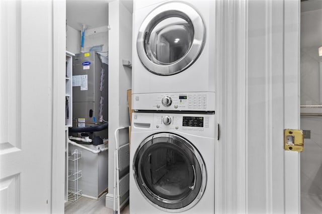 clothes washing area with water heater, stacked washer and clothes dryer, and light wood-type flooring